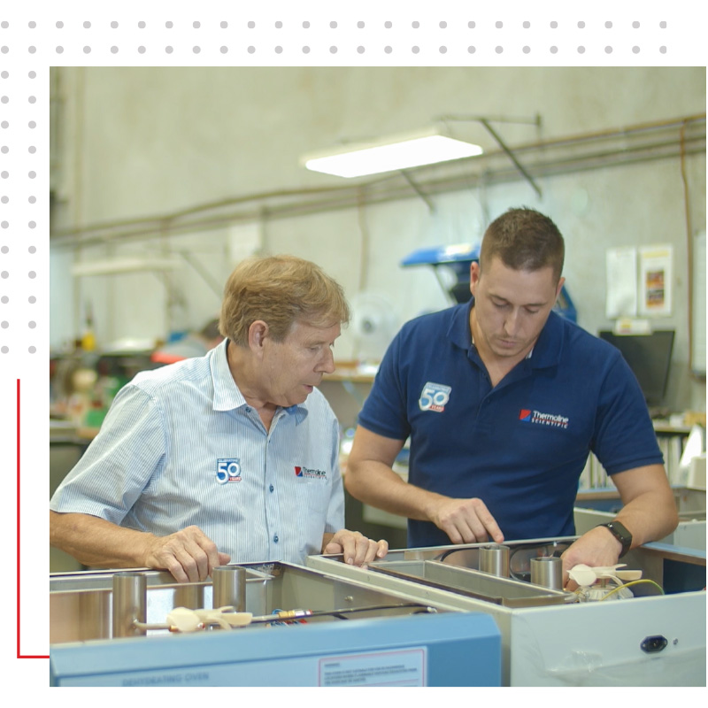 Two technicians in a workshop working together on assembling or repairing laboratory equipment.