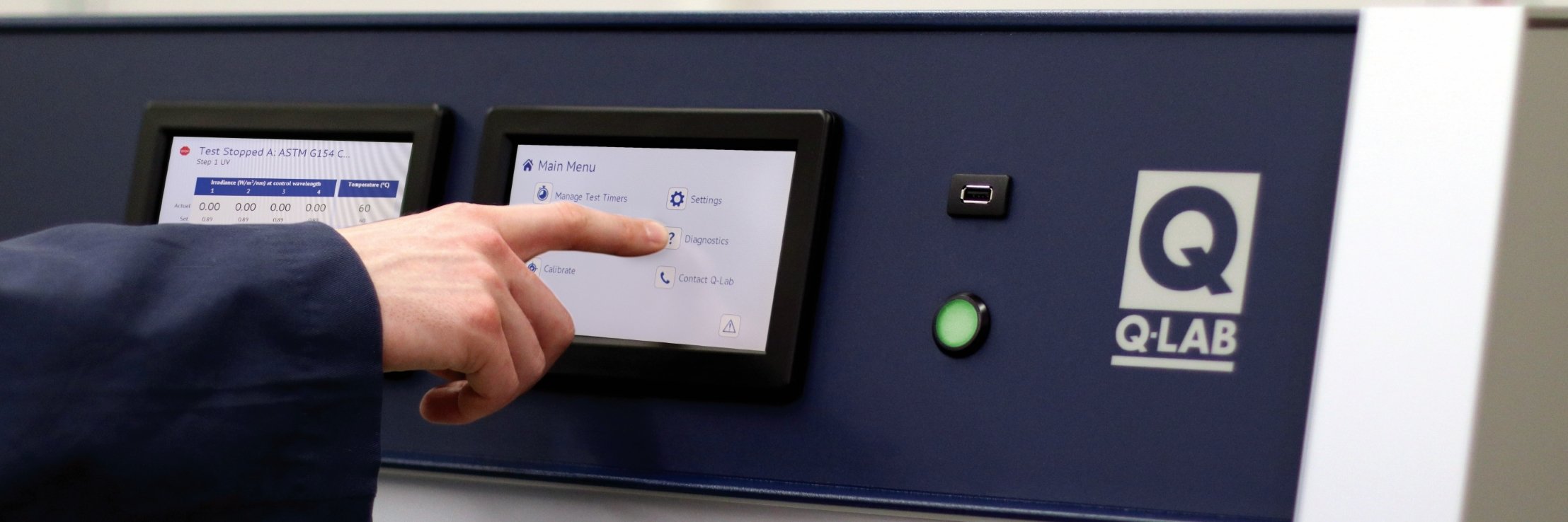 Close-up of a person interacting with the touchscreen controls of a Q-Lab testing equipment, displaying various settings and diagnostic options.